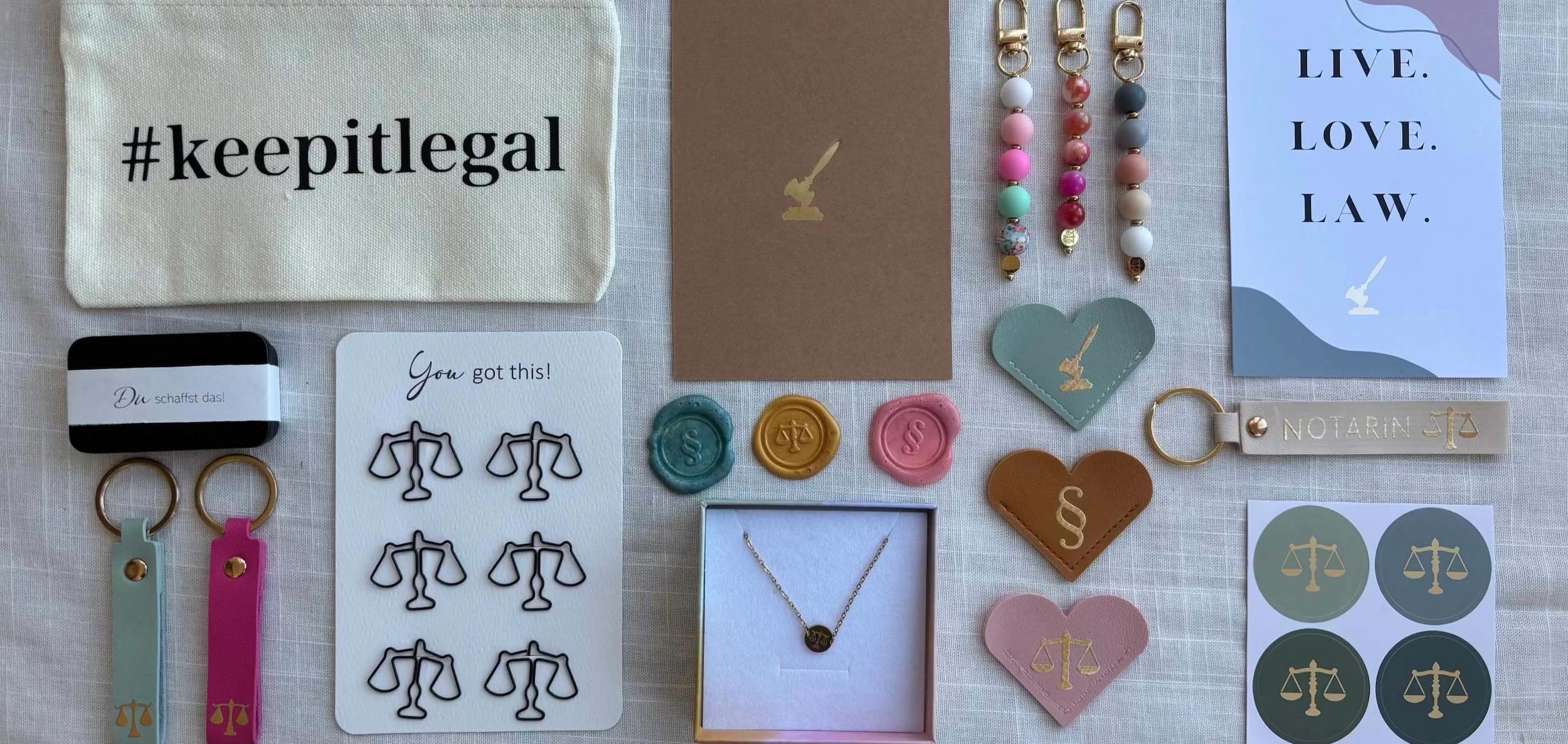 Übersicht einiger Produkte z.B. Jura Postkarten, Juristische Schlüsselanhänger, Büroklammern in Waageform