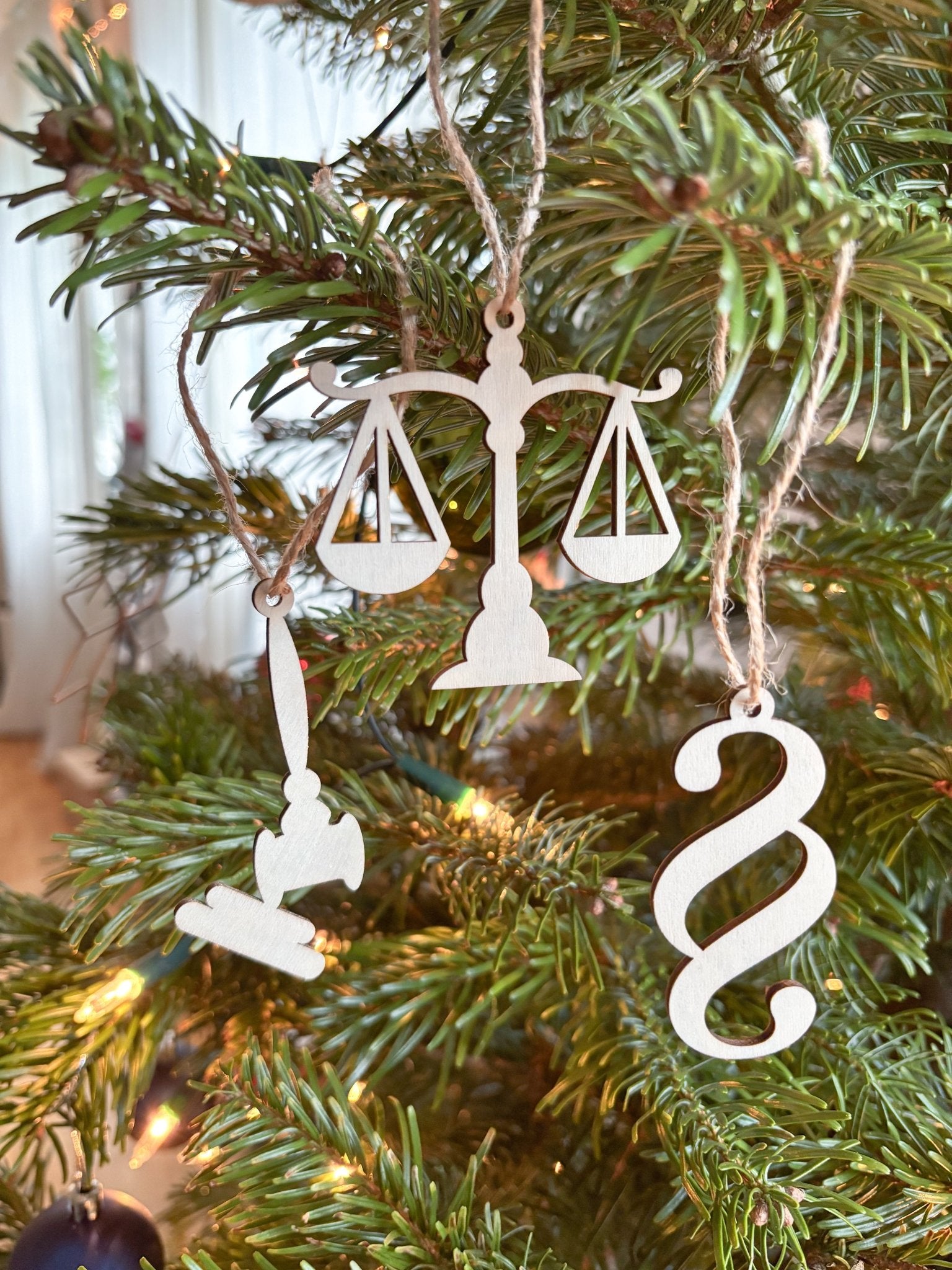 Drei Christbaumanhänger Waage, Richterhammer und Paragraph aus Holz an einem Tannenbaum hängend.